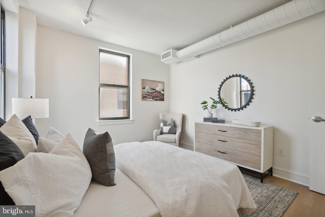 bedroom with rail lighting and light hardwood / wood-style flooring