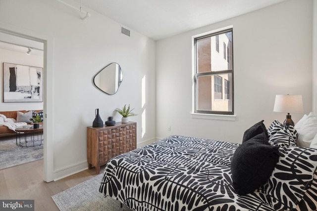 bedroom with multiple windows, track lighting, and light hardwood / wood-style floors