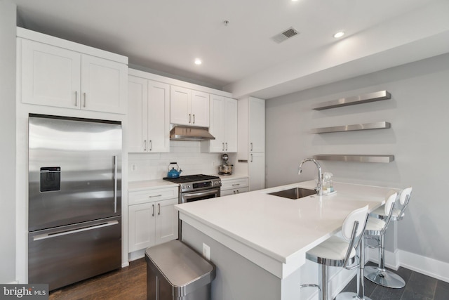 kitchen with appliances with stainless steel finishes, white cabinetry, decorative backsplash, a kitchen breakfast bar, and sink