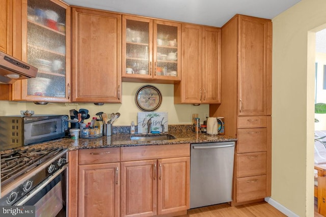 kitchen with range with gas cooktop, dark stone countertops, light hardwood / wood-style floors, stainless steel dishwasher, and sink