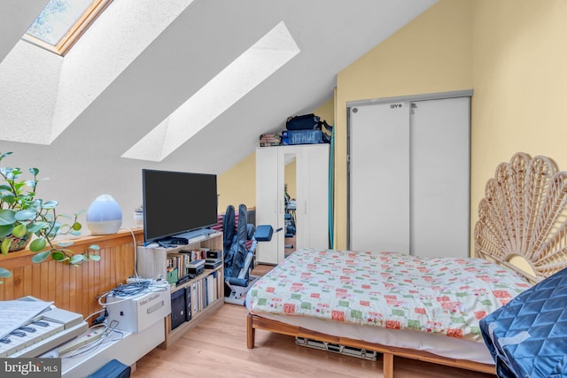 bedroom featuring light wood-type flooring, a closet, and lofted ceiling with skylight