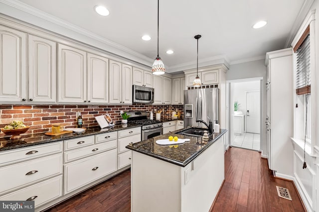 kitchen with sink, hanging light fixtures, a center island with sink, appliances with stainless steel finishes, and dark stone counters