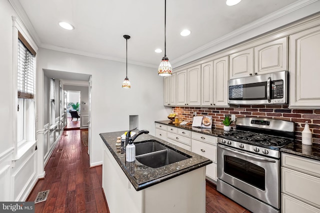 kitchen featuring sink, hanging light fixtures, a center island with sink, dark stone countertops, and stainless steel appliances