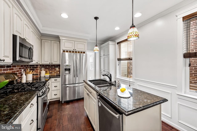 kitchen with sink, appliances with stainless steel finishes, hanging light fixtures, an island with sink, and dark stone counters