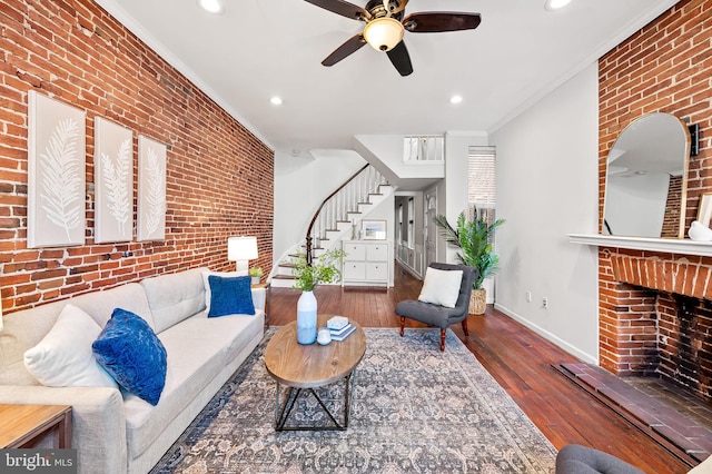 living room featuring brick wall, a fireplace, hardwood / wood-style flooring, ornamental molding, and ceiling fan