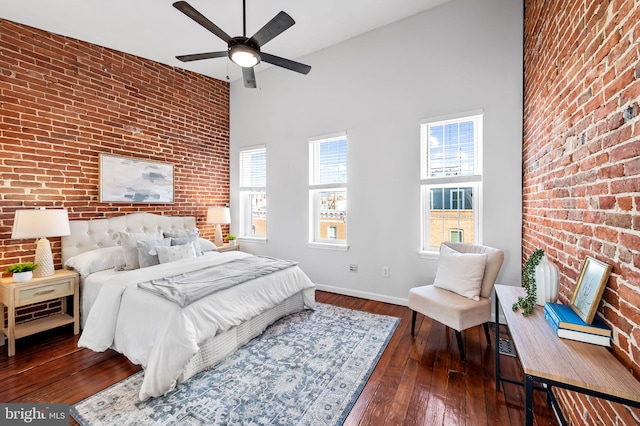 bedroom featuring dark hardwood / wood-style flooring, a towering ceiling, and brick wall