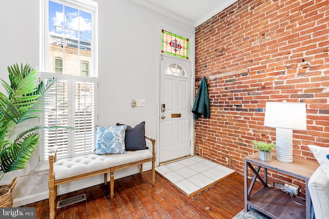 foyer entrance with hardwood / wood-style flooring, plenty of natural light, ornamental molding, and brick wall