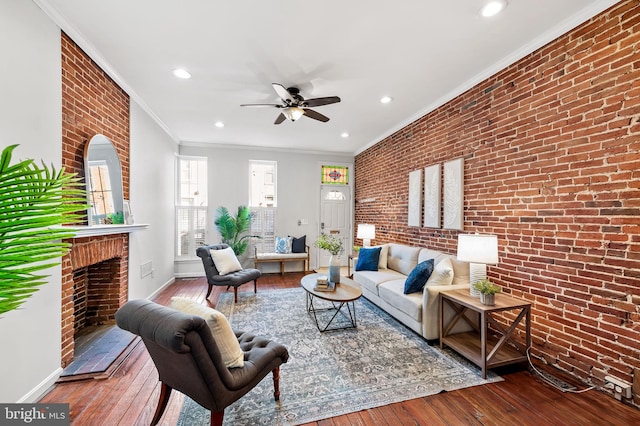 living room with hardwood / wood-style flooring, ceiling fan, ornamental molding, brick wall, and a brick fireplace