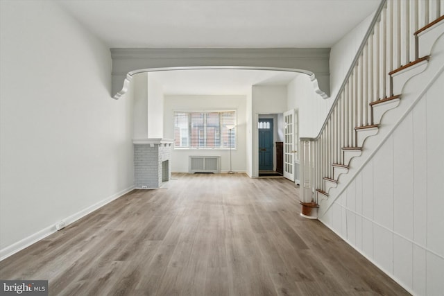 unfurnished living room featuring radiator, a brick fireplace, and hardwood / wood-style flooring