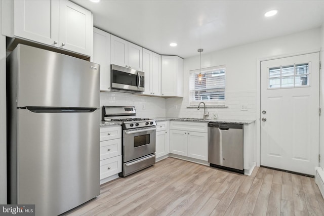 kitchen with stainless steel appliances, pendant lighting, white cabinets, light stone counters, and sink