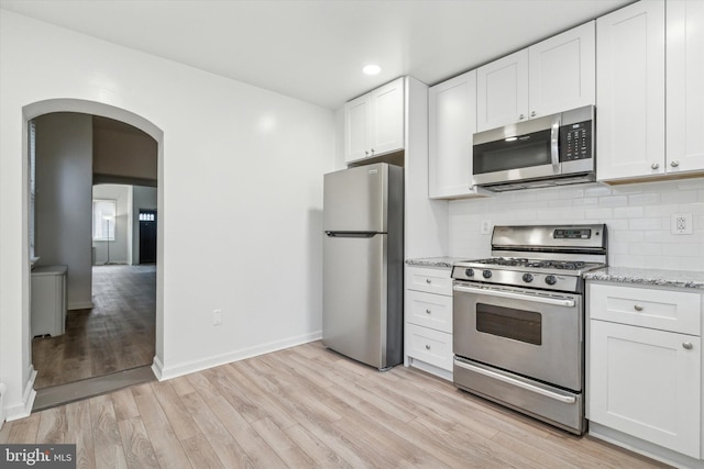 kitchen with tasteful backsplash, light hardwood / wood-style floors, white cabinetry, light stone countertops, and stainless steel appliances