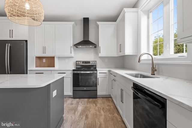 kitchen with white cabinets, wall chimney exhaust hood, stainless steel appliances, sink, and hanging light fixtures