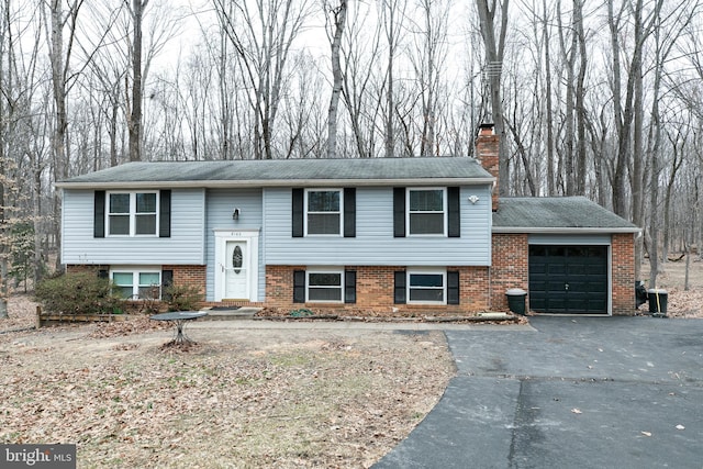 split foyer home featuring driveway, brick siding, a chimney, and an attached garage