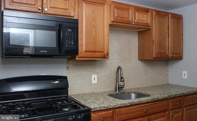 kitchen with sink, backsplash, light stone counters, and black appliances