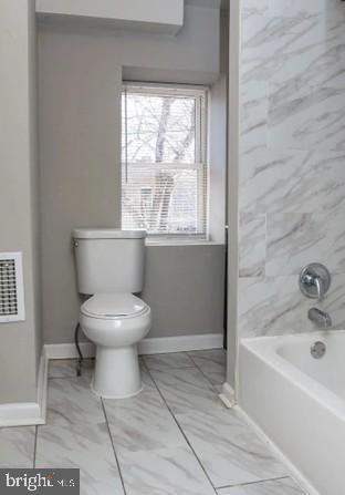 bathroom featuring toilet, a healthy amount of sunlight, and washtub / shower combination