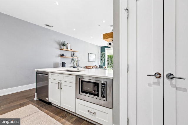 kitchen with appliances with stainless steel finishes, white cabinetry, dark hardwood / wood-style flooring, sink, and kitchen peninsula