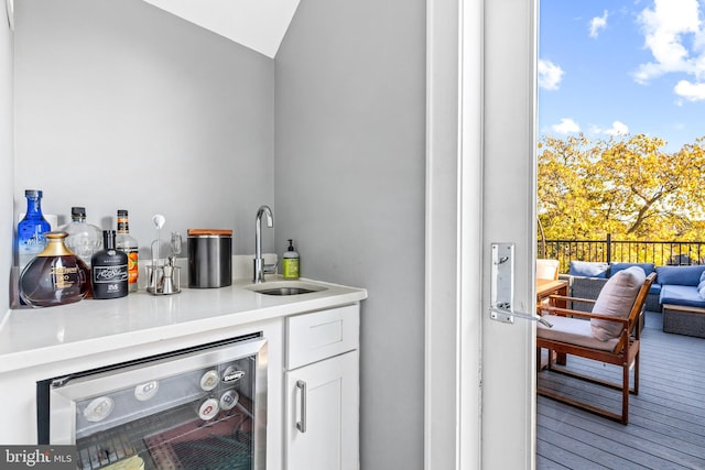 bar with sink, white cabinetry, wine cooler, and lofted ceiling