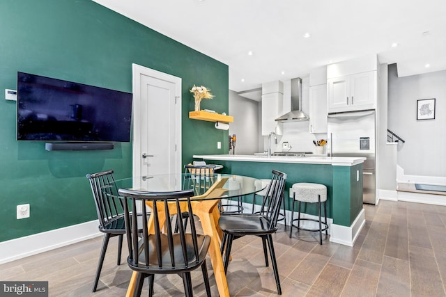 kitchen featuring white cabinets, wall chimney exhaust hood, a kitchen bar, stainless steel built in refrigerator, and a center island with sink