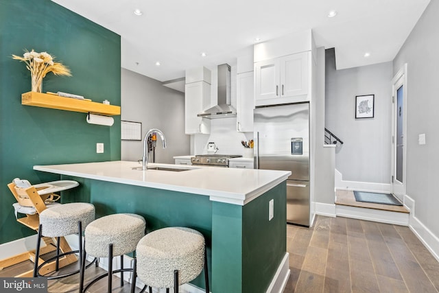 kitchen featuring wall chimney exhaust hood, white cabinetry, stainless steel appliances, sink, and a breakfast bar area