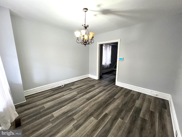 spare room with dark wood-type flooring and a notable chandelier