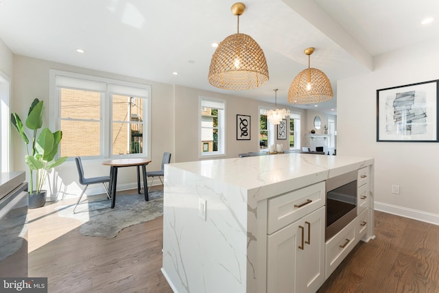 kitchen with white cabinetry, hanging light fixtures, light stone counters, wood-type flooring, and a kitchen island