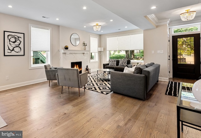 living room with a notable chandelier, crown molding, a fireplace, and light wood-type flooring