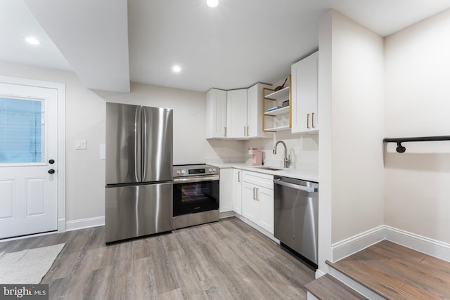 kitchen with sink, light wood-type flooring, white cabinets, and appliances with stainless steel finishes