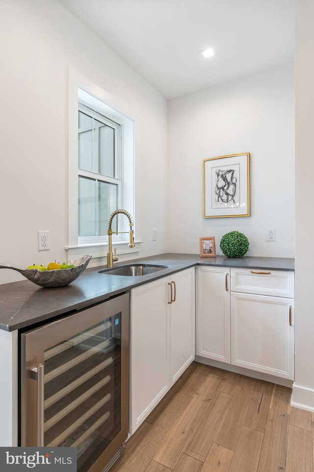 bar featuring sink, beverage cooler, and white cabinetry