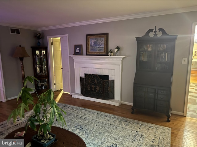 living room with a brick fireplace, ornamental molding, and hardwood / wood-style flooring