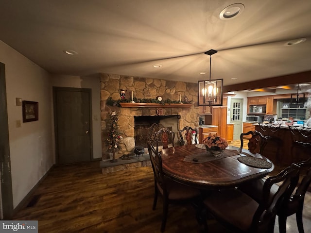 dining room featuring hardwood / wood-style flooring, a notable chandelier, and a stone fireplace