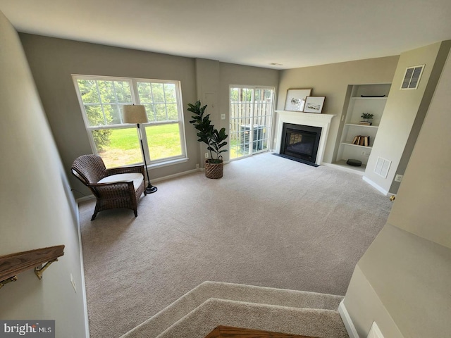 carpeted living area featuring a fireplace with flush hearth, baseboards, visible vents, and built in shelves