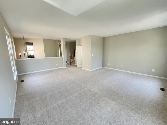 carpeted empty room with an inviting chandelier, stairway, visible vents, and baseboards