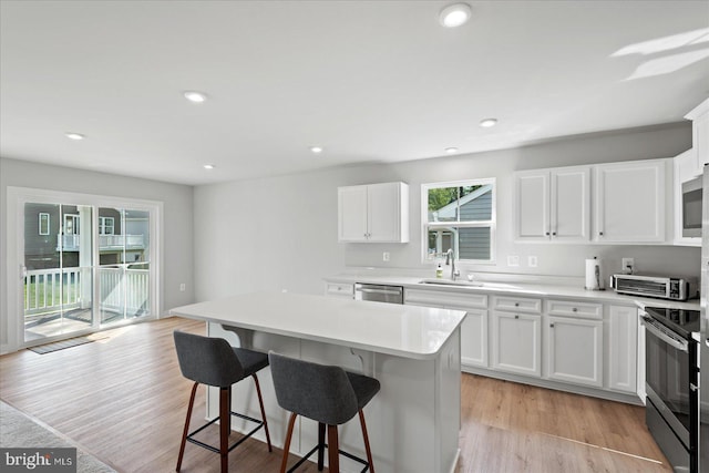 kitchen with appliances with stainless steel finishes, a kitchen island, white cabinetry, sink, and light hardwood / wood-style flooring