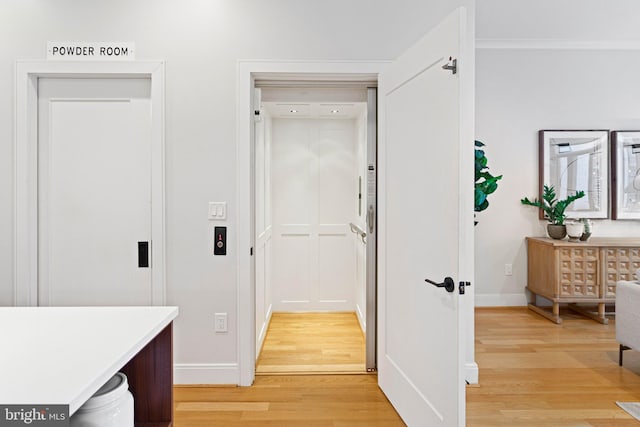 hallway with elevator, light wood-type flooring, and ornamental molding