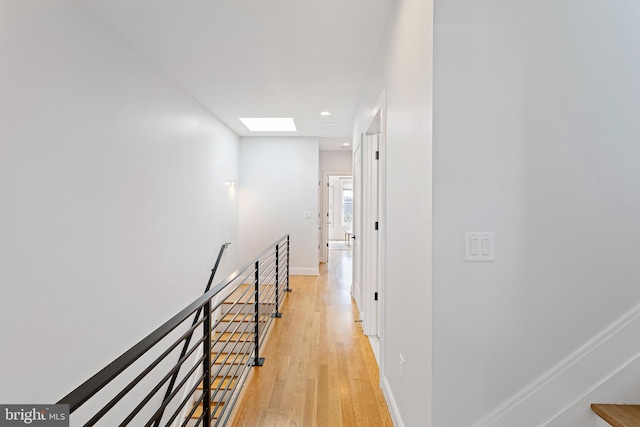 corridor with light wood-type flooring and a skylight