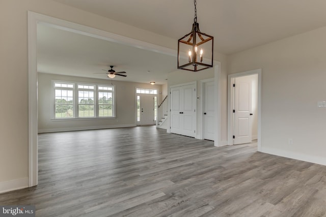 unfurnished living room featuring ceiling fan with notable chandelier and light hardwood / wood-style flooring