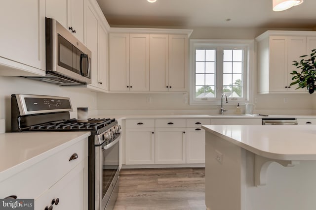 kitchen with white cabinetry, a breakfast bar area, stainless steel appliances, light hardwood / wood-style flooring, and sink