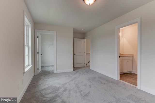 unfurnished bedroom with ensuite bath, light colored carpet, a closet, and a spacious closet