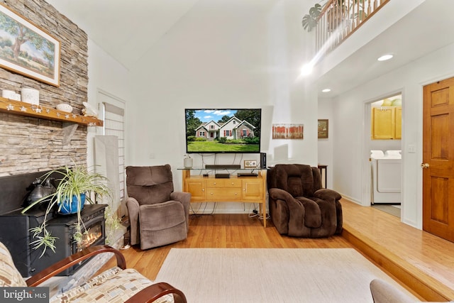 living room featuring a fireplace, a high ceiling, washing machine and clothes dryer, and light hardwood / wood-style flooring