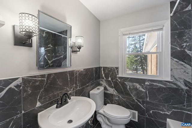 bathroom with toilet, tile walls, and sink