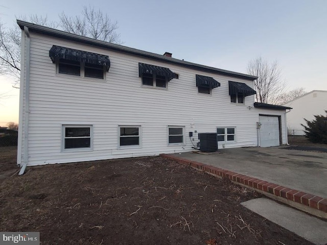 back house at dusk with a garage, central AC, and a patio area