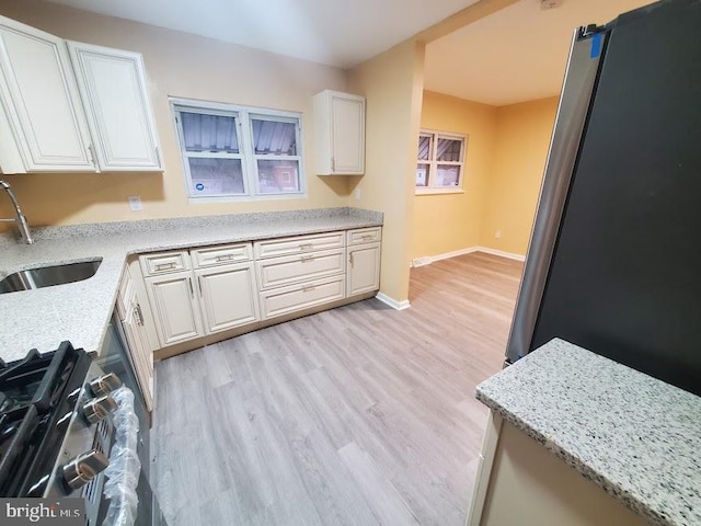 kitchen featuring light hardwood / wood-style floors, light stone countertops, stainless steel stove, white cabinets, and sink