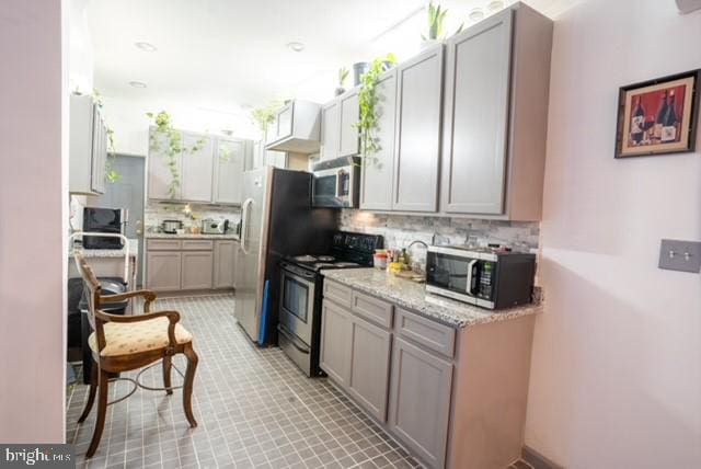 kitchen with light stone countertops, appliances with stainless steel finishes, gray cabinets, and tasteful backsplash