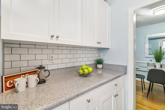 kitchen with tasteful backsplash, light wood-type flooring, light stone counters, and white cabinetry