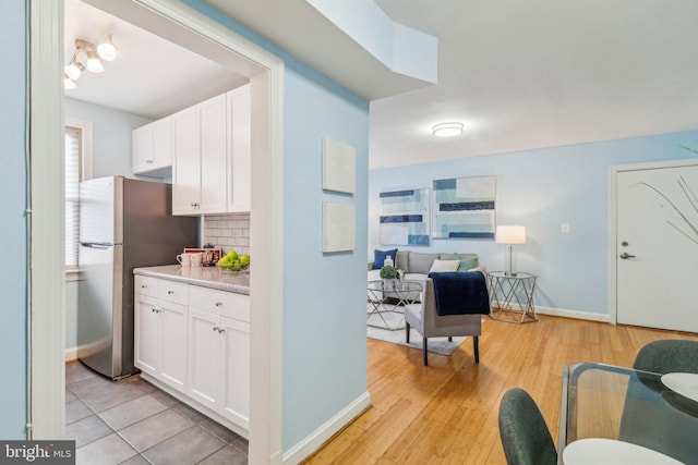 kitchen featuring decorative backsplash, light hardwood / wood-style floors, white cabinets, and stainless steel refrigerator