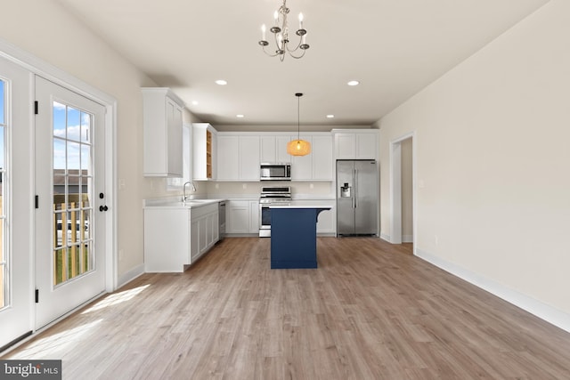 kitchen featuring decorative light fixtures, a kitchen island, white cabinetry, light hardwood / wood-style flooring, and stainless steel appliances