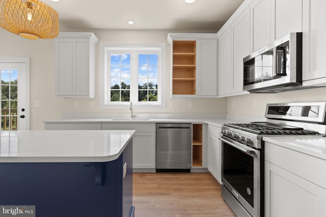 kitchen with decorative light fixtures, sink, white cabinetry, light hardwood / wood-style flooring, and appliances with stainless steel finishes