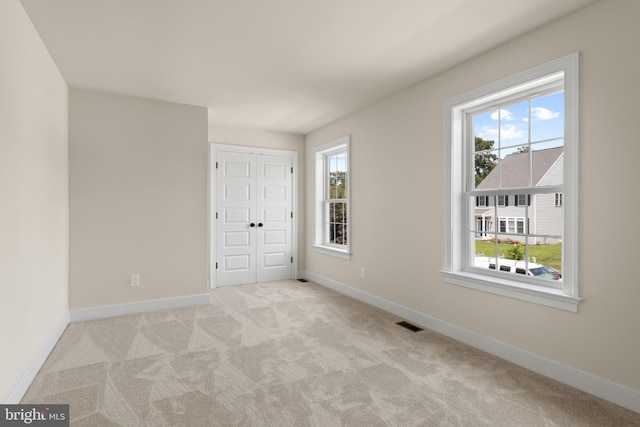 unfurnished bedroom with light colored carpet, a closet, and multiple windows