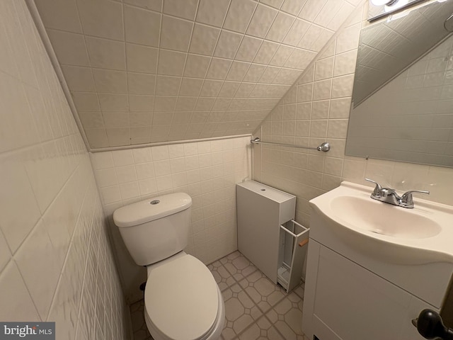 bathroom with toilet, vanity, tile walls, vaulted ceiling, and tile patterned floors