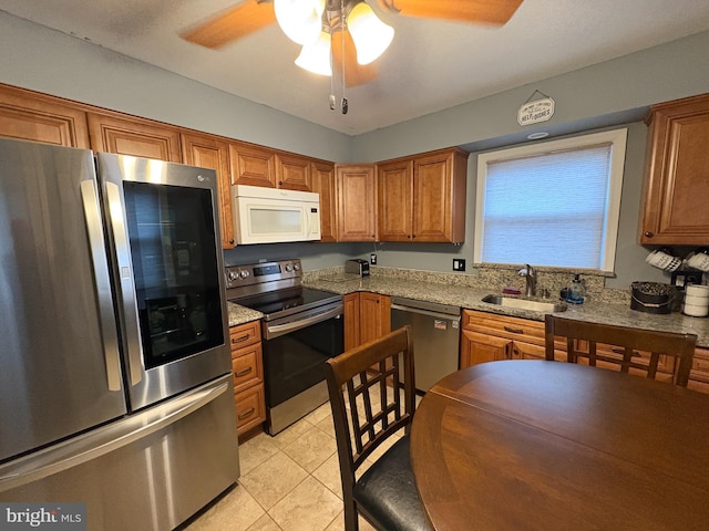 kitchen featuring light stone countertops, stainless steel appliances, sink, ceiling fan, and light tile patterned floors